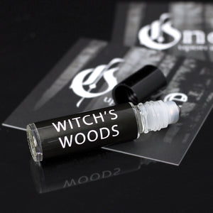Perfume that smells like leaves in a glass roller vial with a black label that says "witch's woods" in white font.