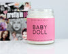 90s theme scented candle with a pink label and black text that says Baby Doll infront of a collage of 90s grunge music icons; courtney love, shirley manson