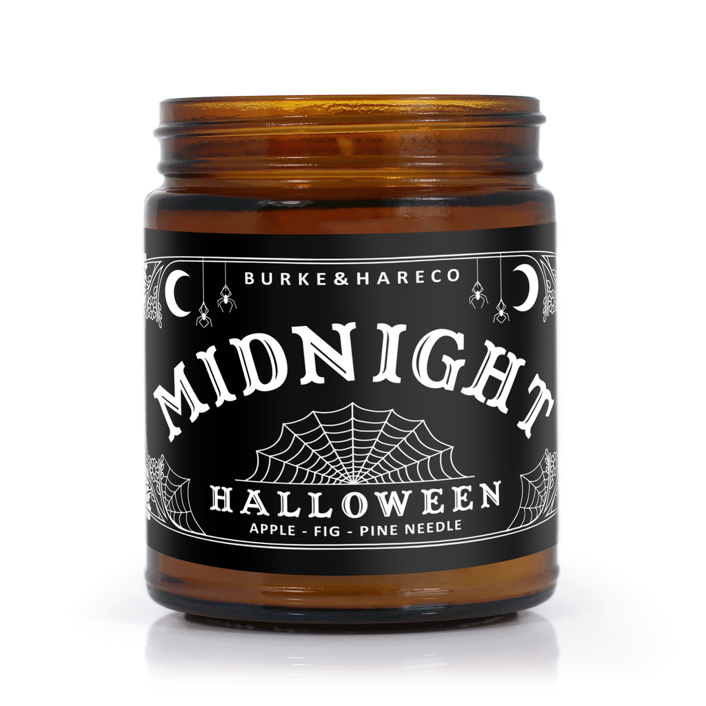 halloween scented candle in an amber jar with a black label that has spider webs and little moons on it. Scent notes listed apple, fig and pine needle.