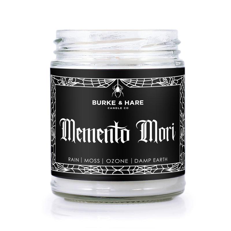 Petrichor Scented candle with a black gothic label that has spiderweb border details and says Memento Mori in gothic font. 