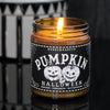 Halloween soy candle in an amber jar lit in a dark room. The candle label is black with white jack o lanterns on it and says Pumpkin in ouija board font.