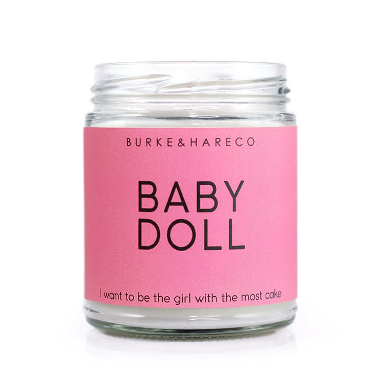 90s themed scented candle with a pink label and black text that says Baby Doll  and "i want to be the girl with the most cake"