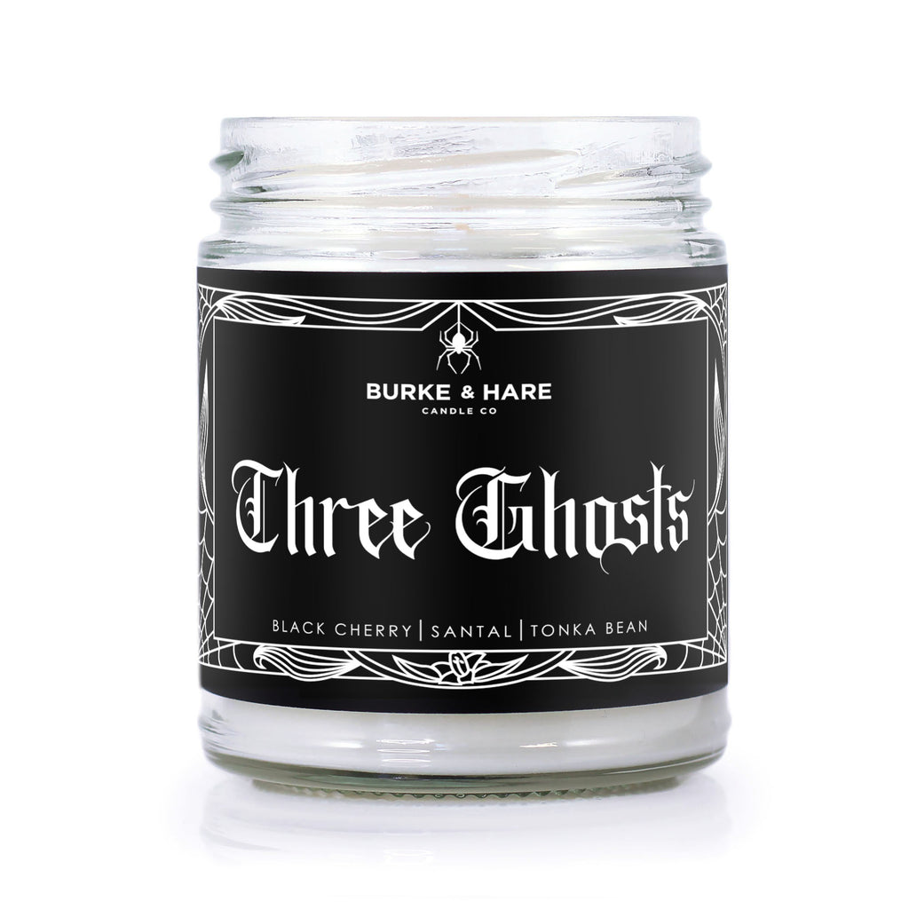 Cherry scented christmas candle with black label and white text that reads "Three Ghosts" in gothic font. Label has a filigree border with a spider.