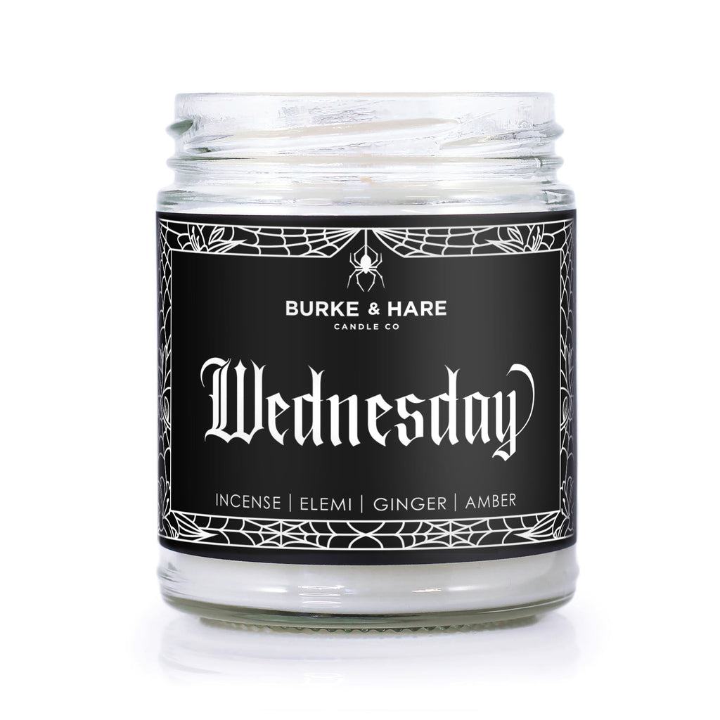 Addams Family inspired candle with a black label and spiderweb border that reads Wednesday in gothic font.