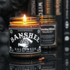 a Lit witchy scented candle with a black label with the graphic of witchy hands holding a crystal ball on it and says "Banshee" 