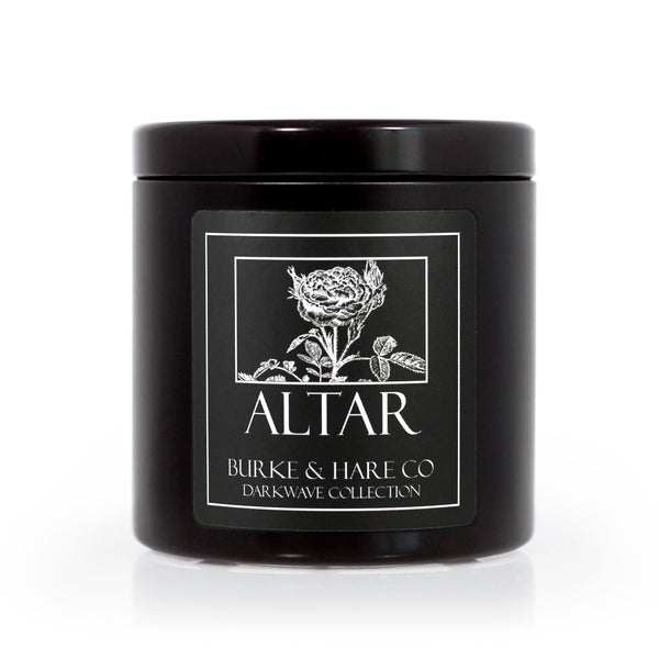 Rose scented black candle in a black tin with  a white rose illustration on the label and white text that says Altar. Vampire candles