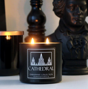 A lit church themed scented candle in a black tin with an illustration of a cathedral on the label and white text that says "cathedral"